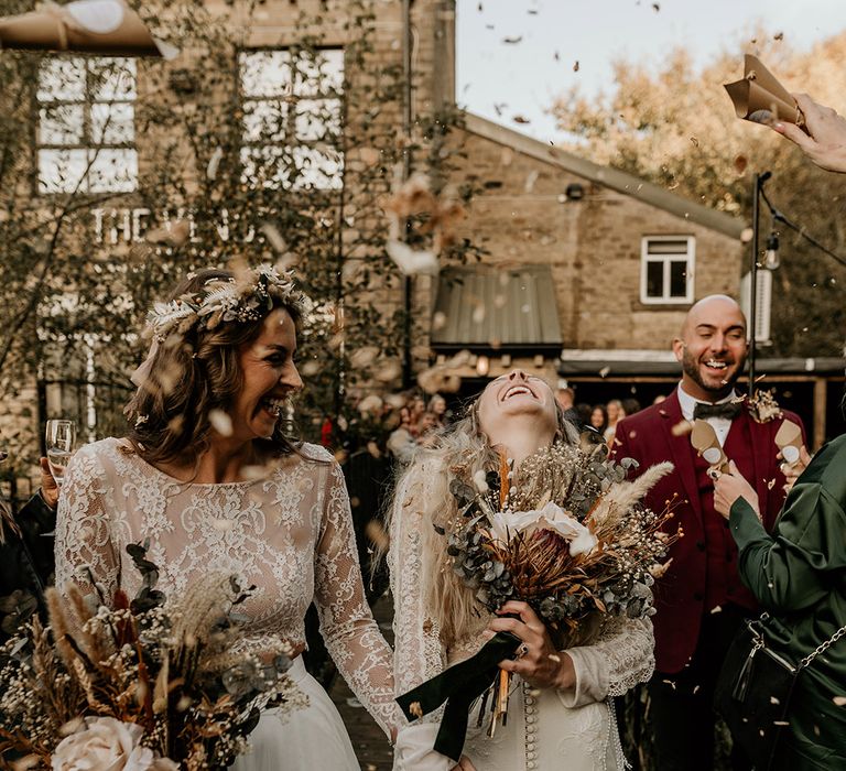 Brides holding hands wearing lace wedding dresses holding dried wedding flower bouquets 