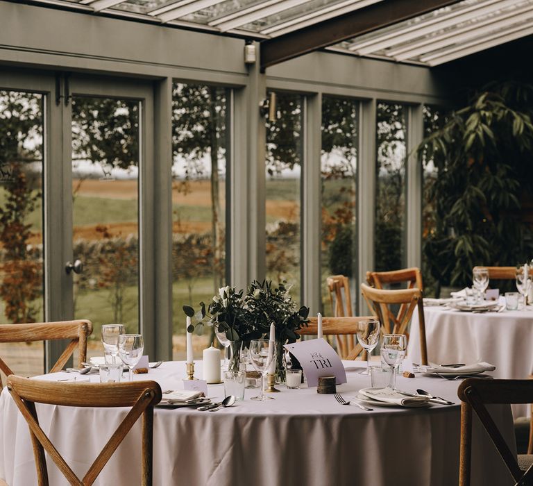 Round tables with white tablecloths, white floral table centrepieces, and white table name signs at Stone Barn rustic wedding venue