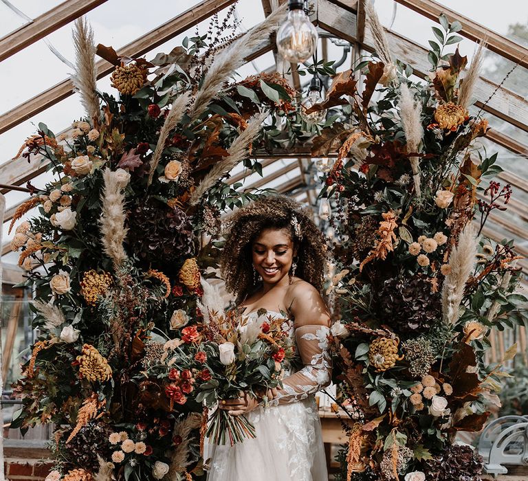 Bride at glasshouse wedding standing in between two autumnal flower columns 