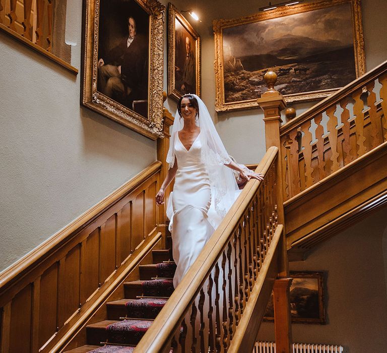 Bride in satin slip wedding dress walking down the stairs to the wedding venue 