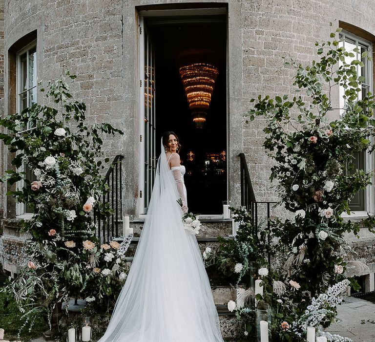 Bride wearing cathedral length veil at chic and elegant wedding with white flower column decorations 