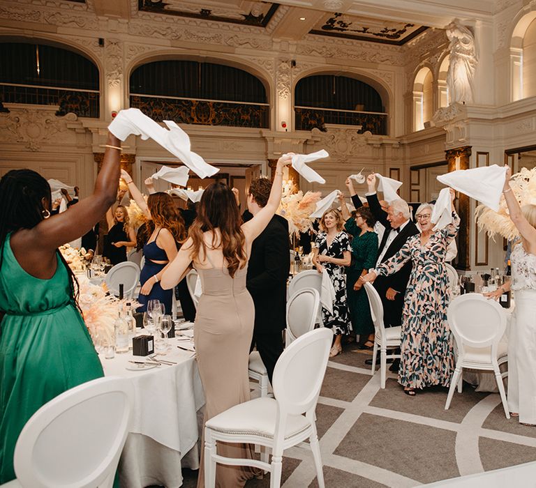 Wedding guests stand and wave their napkins to welcome the bride and groom in the wedding breakfast 