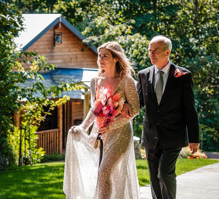 Father of the bride walking the bride in a semi-sheer bespoke wedding dress with sequins and beading down the aisle 