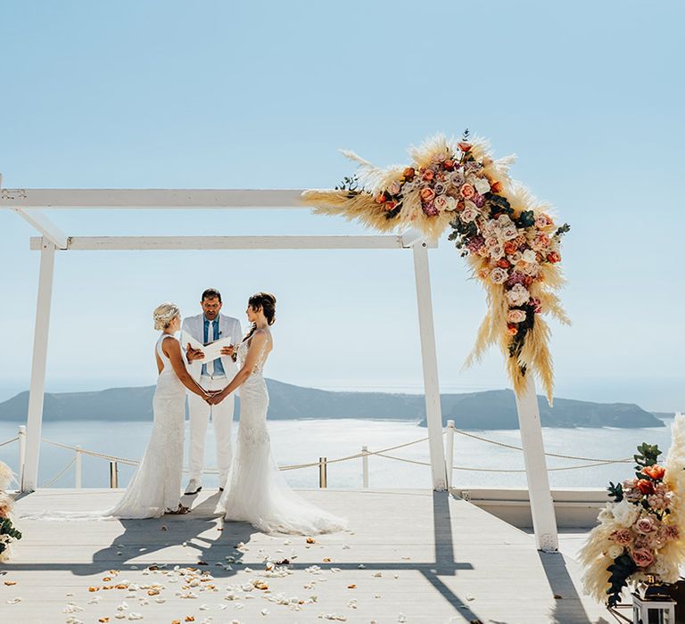 Outdoor wedding ceremony at Santorini destination wedding with two brides in lace gowns