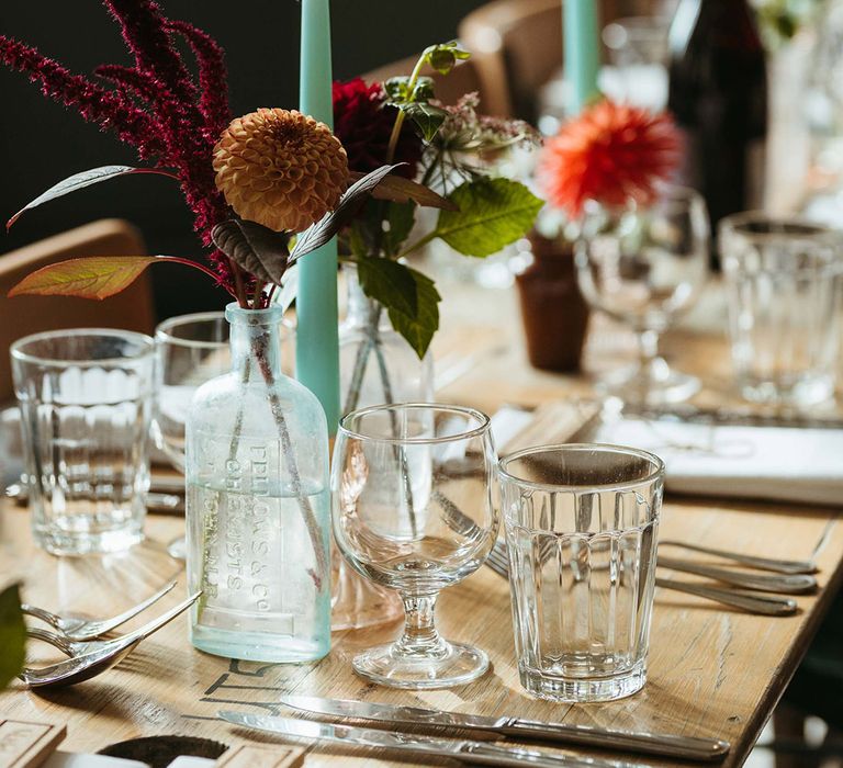 Blue turquoise candles with dark minimalist autumnal seasonal flowers in bud vases 