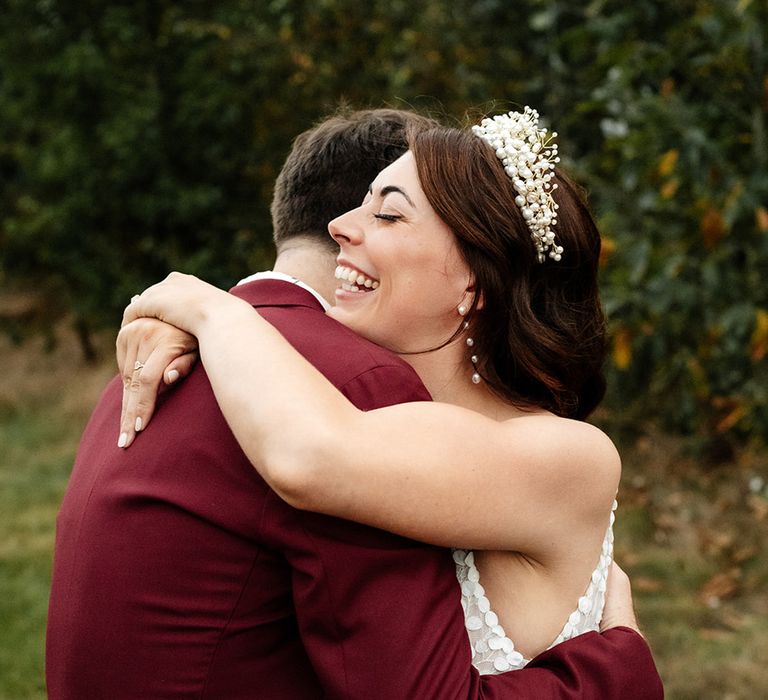 Groom in deep red wedding suit embracing the bride for cute couple portrait 