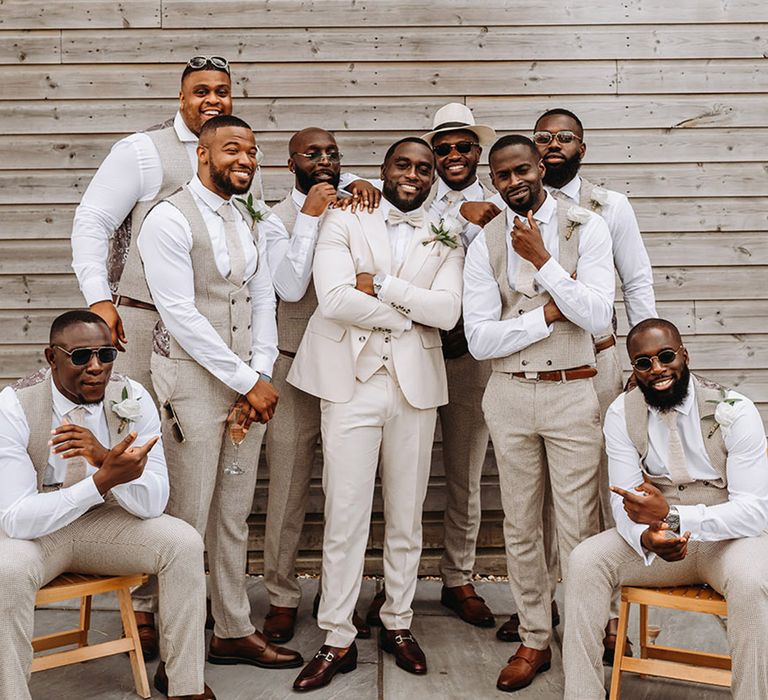 Group wedding photo of the groomsmen and groom wearing cream, beige and white wedding suits for boho luxe wedding 