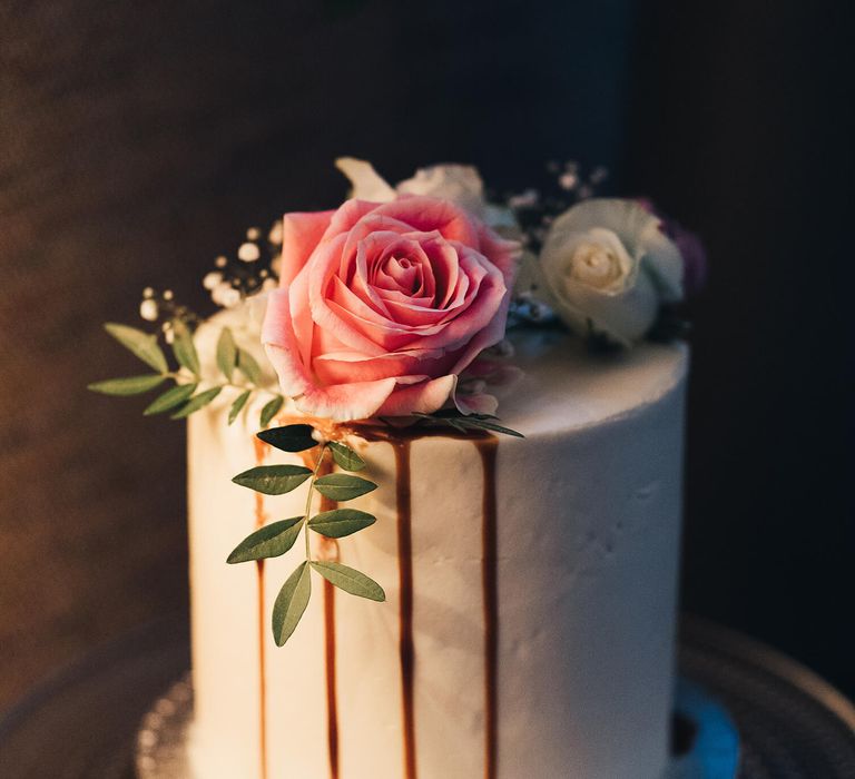 White iced wedding cake with pink rose delicately placed on top with caramel for a drip effect 