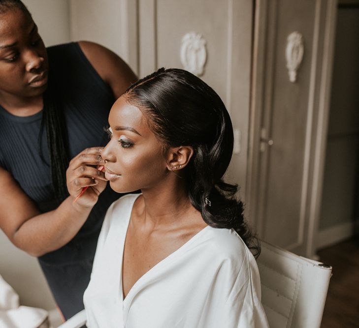 A bride gets her make up done ready for her wedding. She wears a white robe.