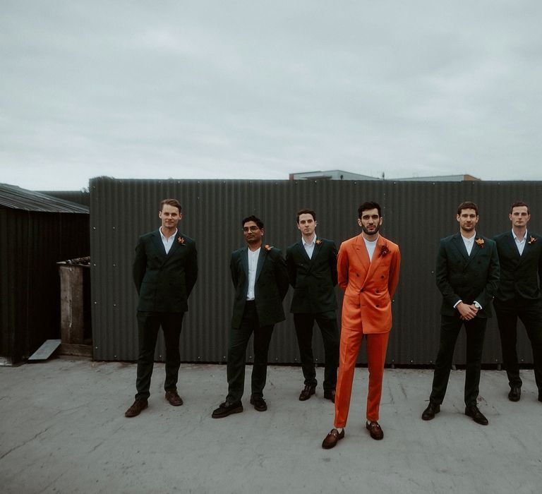 Groomsmen portrait with the Turkish groom in a white t-shirt and double breasted orange suit and the groomsmen in teal green suits. 