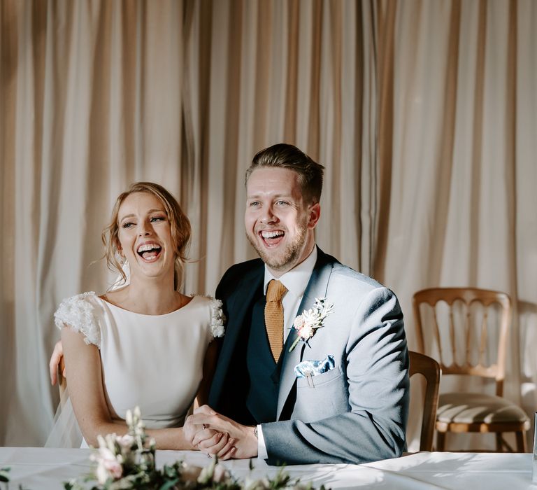 Bride with up do and bearded groom laughing whilst signing the register 