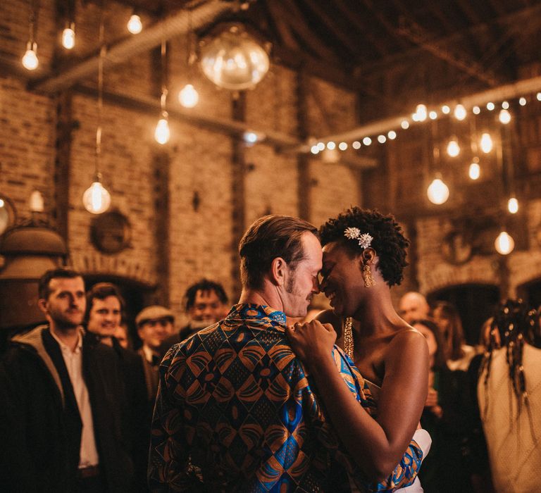 Groom in a blue and gold West African outfit dancing with is bride during the Festoon lit wedding reception 