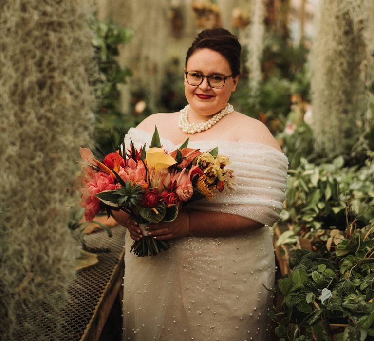 Bride in an off the shoulder wedding dress holding a tropical red, orange and yellow wedding bouquet 