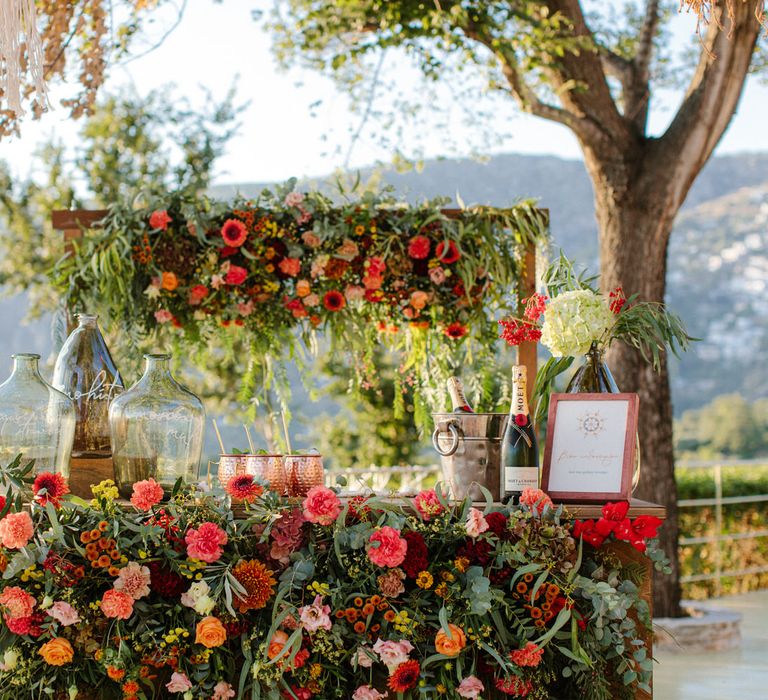 An outdoor cocktail bar covered in flowers, with prosecco, champagne and cocktails