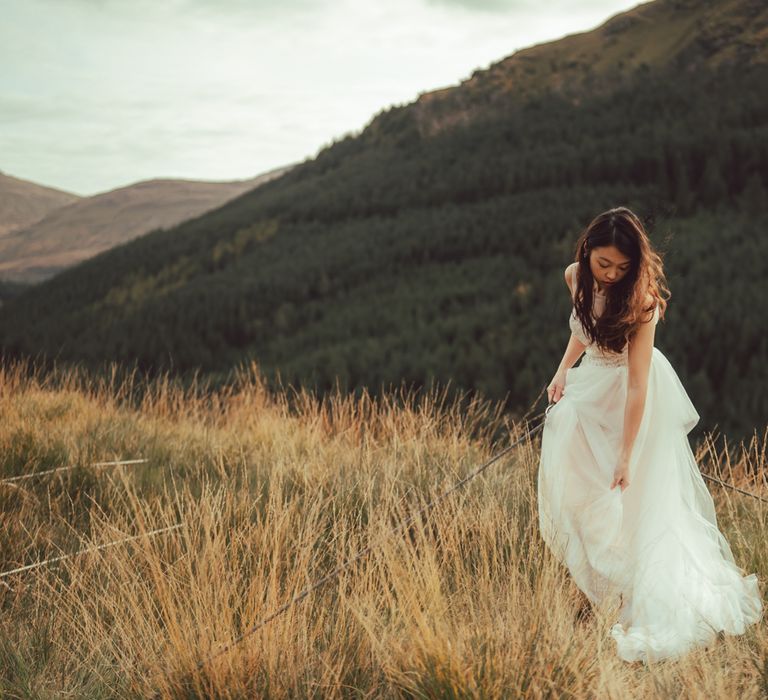 Dark haired girl adjusts her dress as she walks through the Scottish countryside