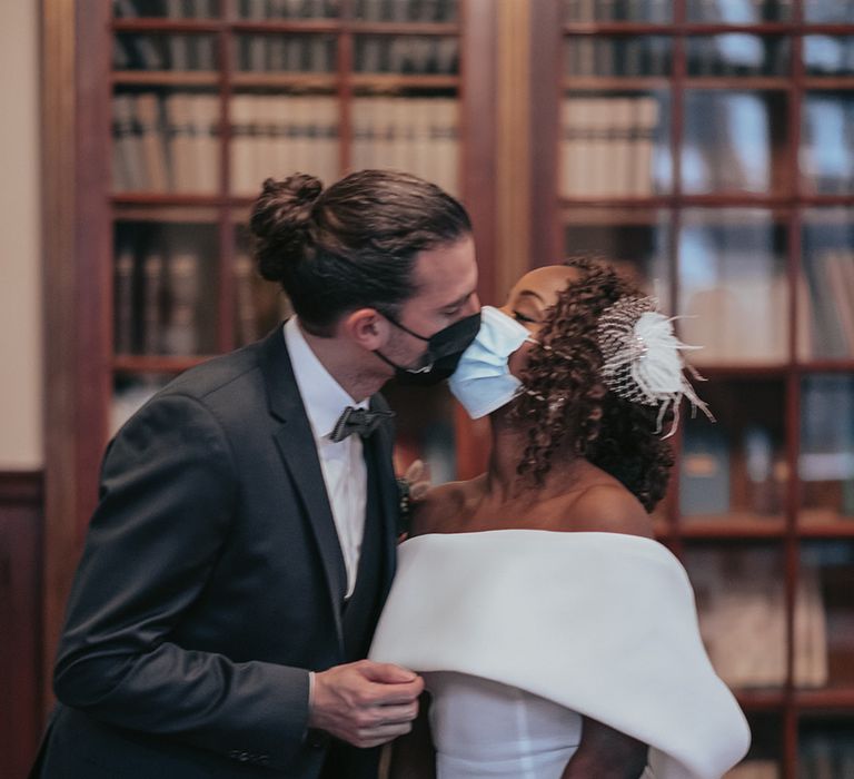 Bride & groom kiss whilst wearing masks