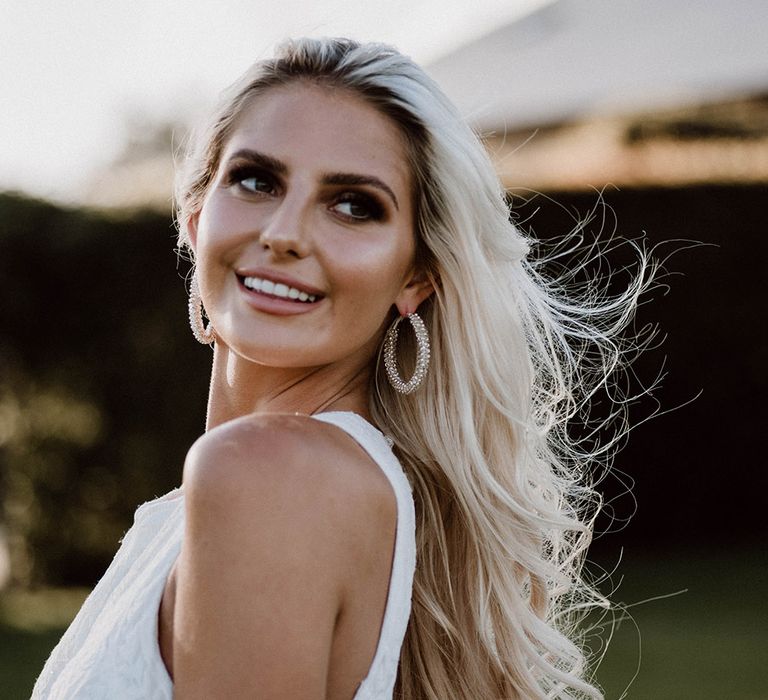 Beautiful blonde bride with smokey eye makeup and lip gloss smiling during golden hour 