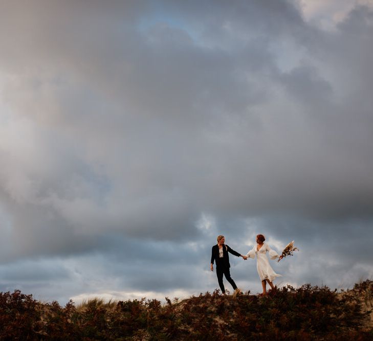 Couple silhouetted on top of dune against overcast sky