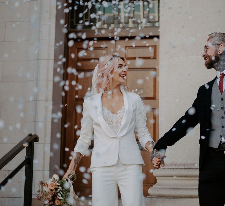 Bride and groom walk down steps as white confetti is thrown