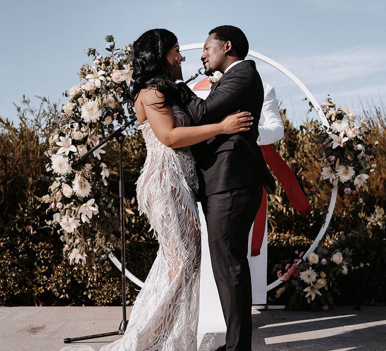 Groom in a tuxedo about to kiss his bride in a feather wedding dress at their outdoor wedding ceremony 