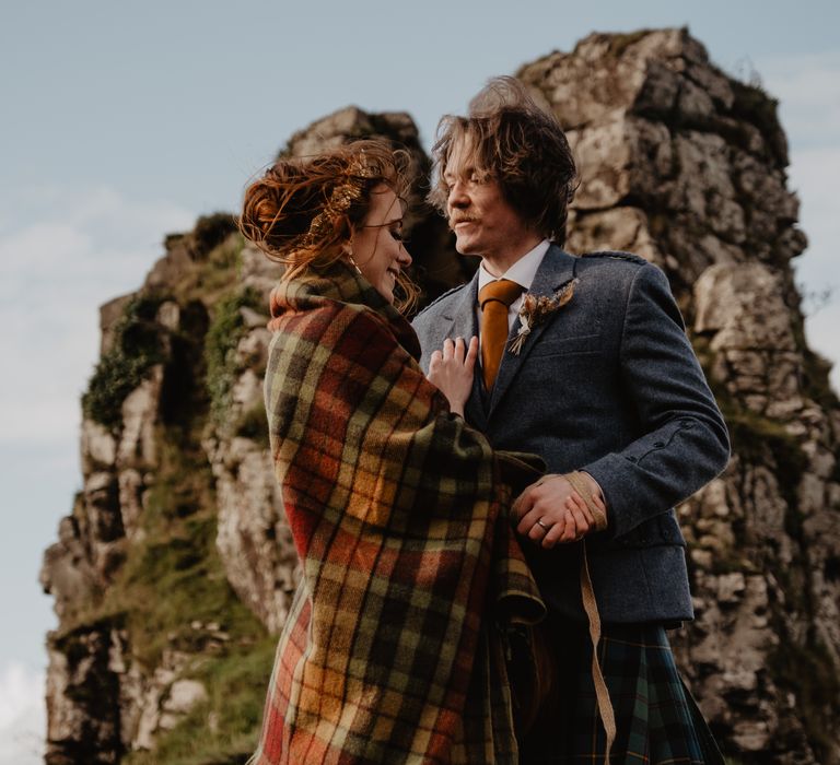 Bride wears tartan blanket around her shoulders as she embraces groom