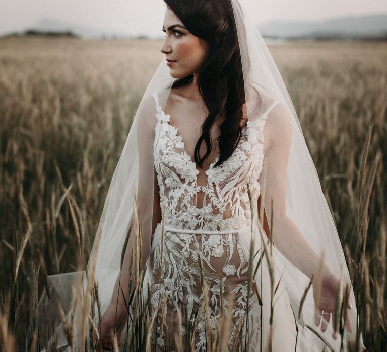 Bride in a field wearing a lace embroidered wedding dress with tulle veil and over skirt