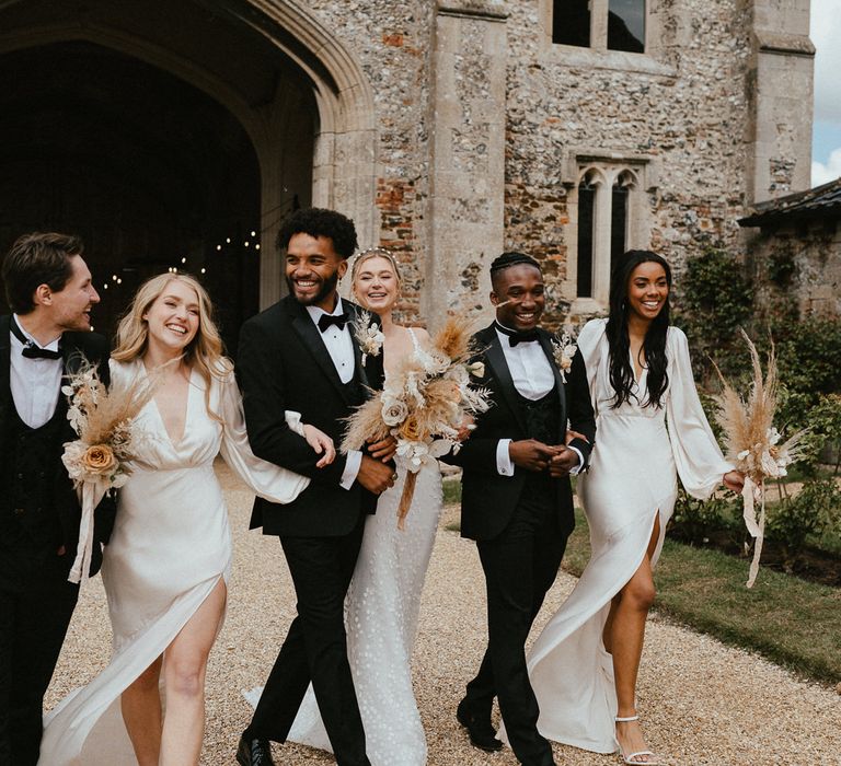 Stylish wedding party walking arm in arm along Pentney Abbey's driveway together 