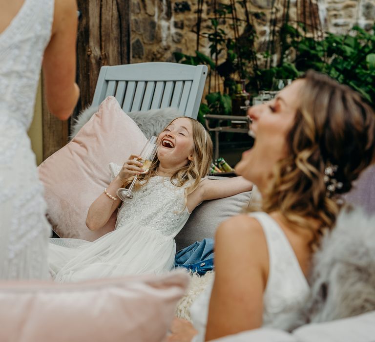 Bridesmaid leans back laughing on sofa whilst holding champagne glass