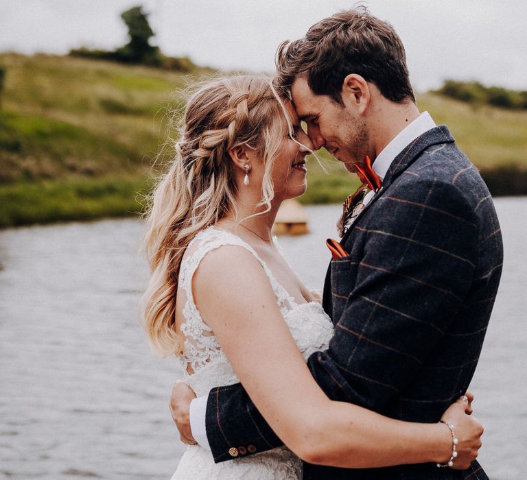 Bride & groom touch foreheads and look lovingly at one another as the lake can be seen behind them and greenery