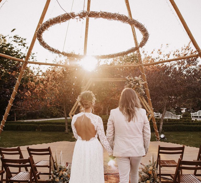 Bride in a open back lace wedding dress and groom in a beige suit at their naked tipi outdoor ceremony 