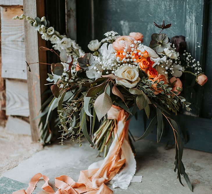 Orange, white and green wedding bouquet with amber ranunculus and spray roses, fluffy white delphiniums, avalanche roses and black centred anemones