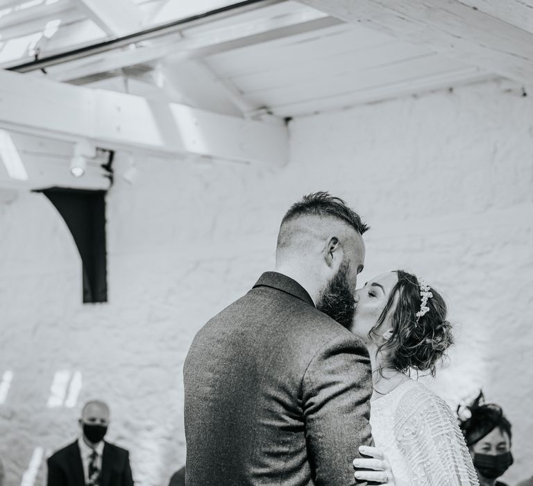 Bride & groom kiss in black & white image as they embrace during wedding ceremony and wedding party applaud 