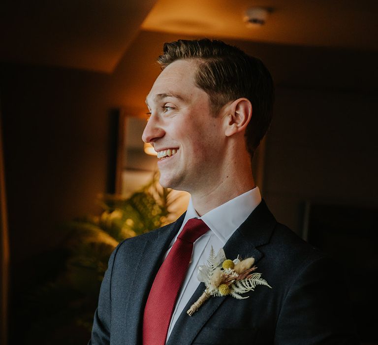 Groom in a black suit with burgundy tie and dried flower buttonhole