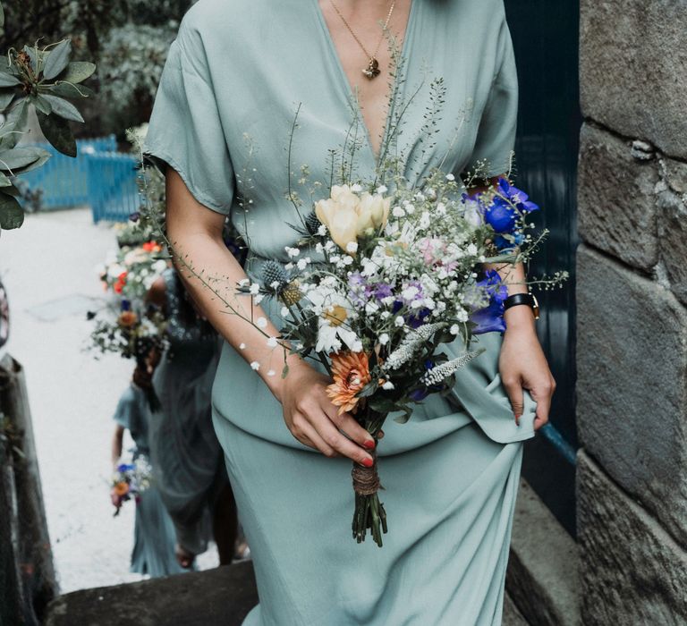 Bridesmaid wears sage green dress whilst carrying handmade floral bouquet