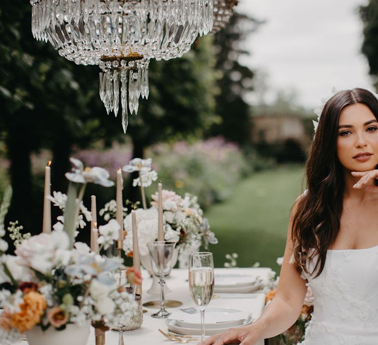 Bride in an appliqué princess wedding dress with straps sitting at the elegant outdoor tablescape 