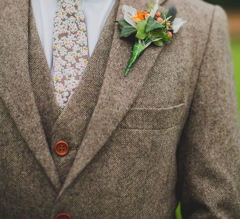 Groom in a brown wool three-piece suit with floral tie and orange flower and foliage buttonhole