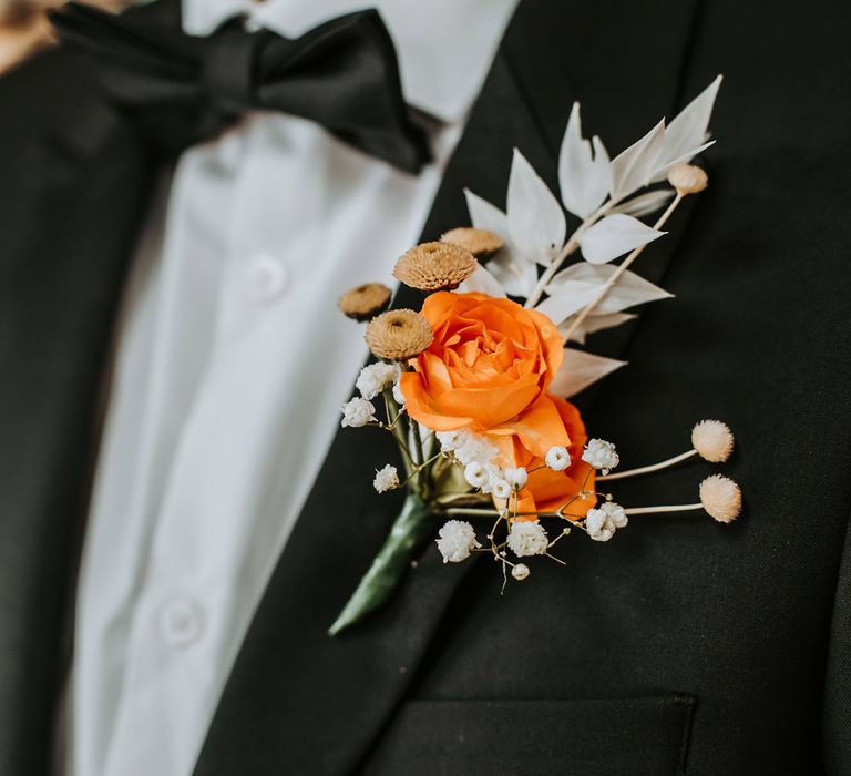 Groom in a Black tuxedo with bright orange ranunculus buttonhole flower 