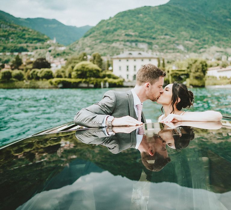 Bride & groom kiss on boat on Lake Como for their elopement wedding ceremony as the Italian countryside fades into the background