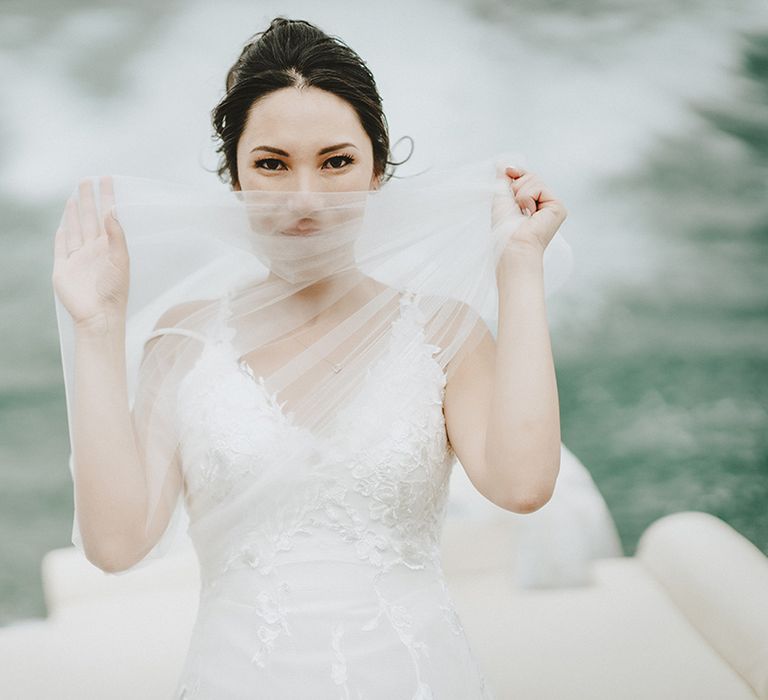 Bride uses her veil to cover her face as her piercing eyes can be seen above as she rides a boat through Lake Como