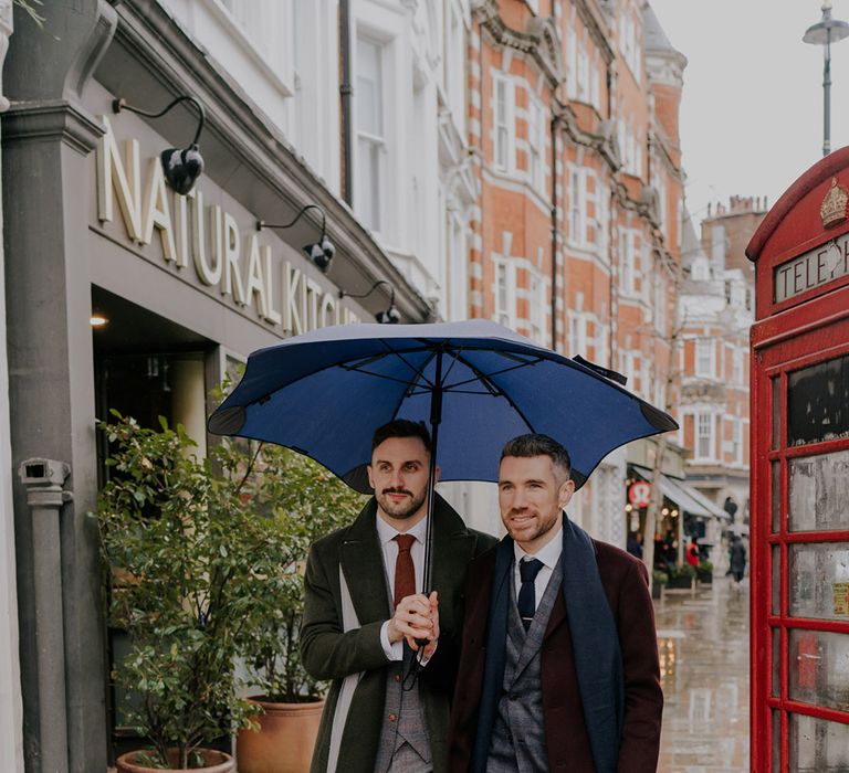 Grooms stand together underneath umbrella on their wedding day within London