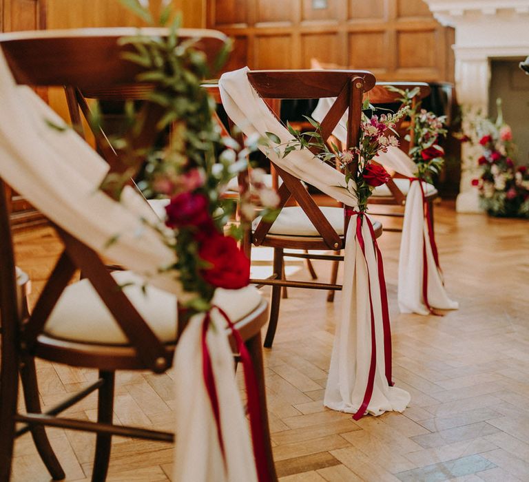 Wooden aisle chairs decorated with white drapes and red rose and foliage decor 