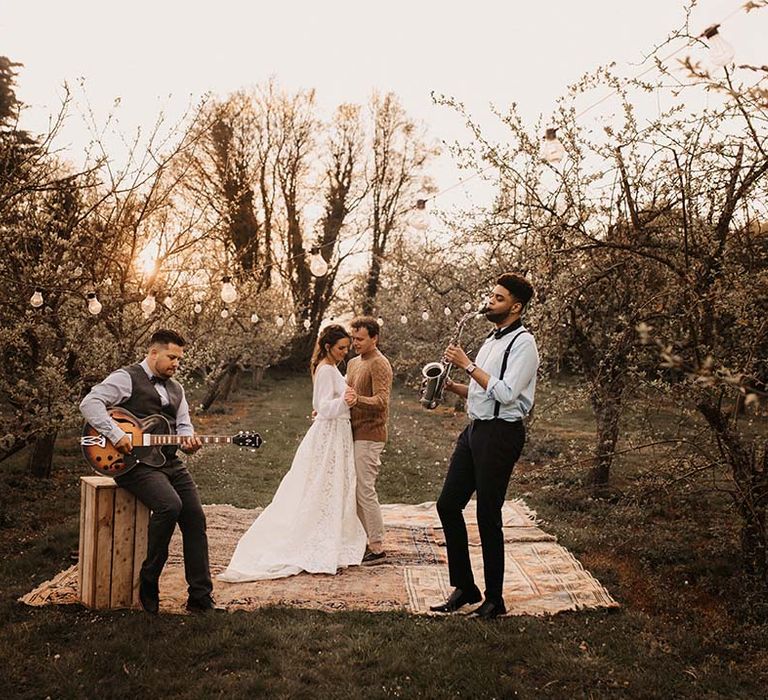 Bride and groom in casual wedding attire having their first dance outside on wool rugs under festoon lights 