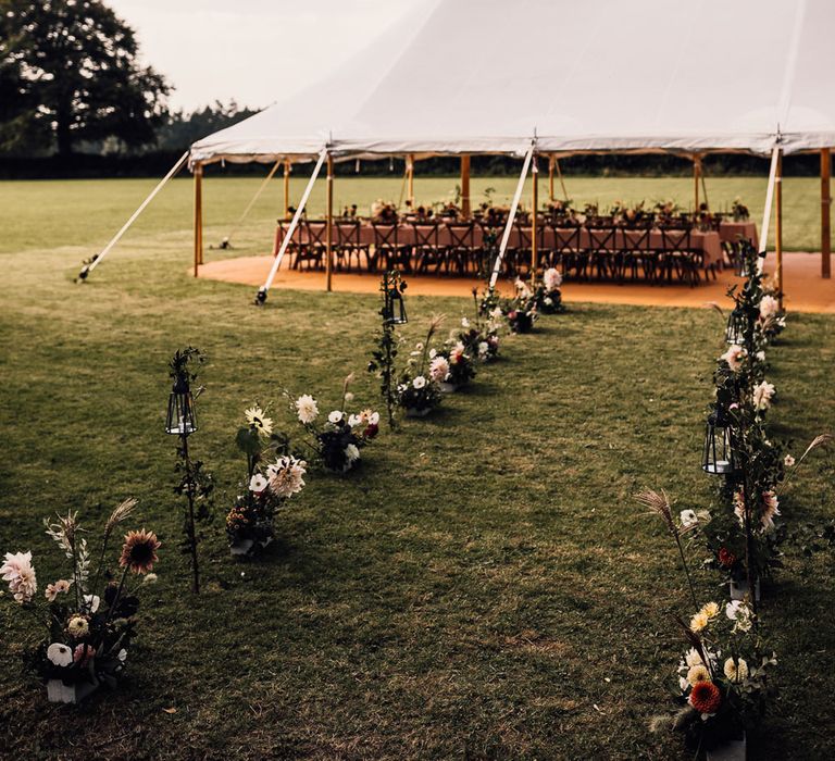 Marquee garden wedding reception in field with long wooden tables with dusky pink tablecloth, wooden chairs and florals for Cornish wedding