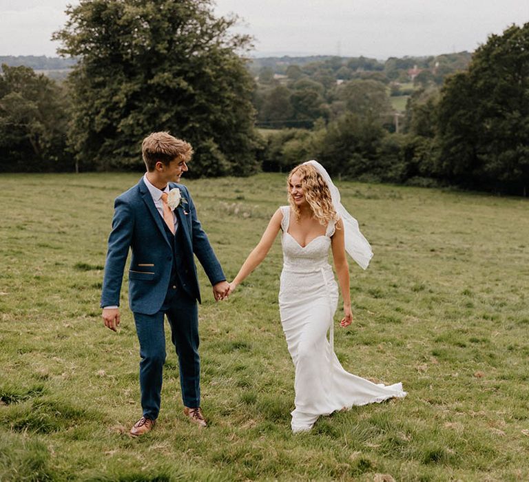 Bride & groom walk across green fields on their wedding day