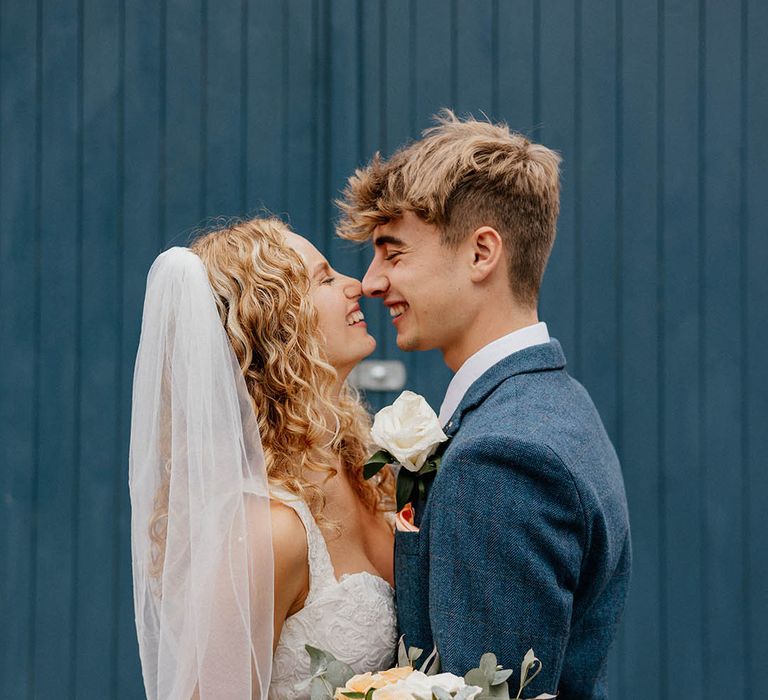 Bride & groom look lovingly at one another outdoors on their wedding day in front of blue door 