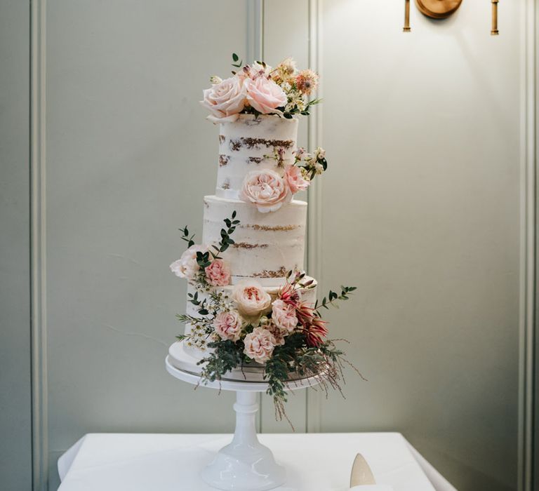 Semi naked wedding cake decorated with flowers on a white cake stand 