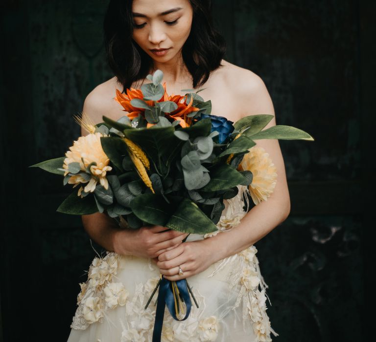 Bride in strapless feathered wedding dress and bridal headpiece holds large tropical bridal bouquet as she stands in doorway at Wellbeing Farm wedding