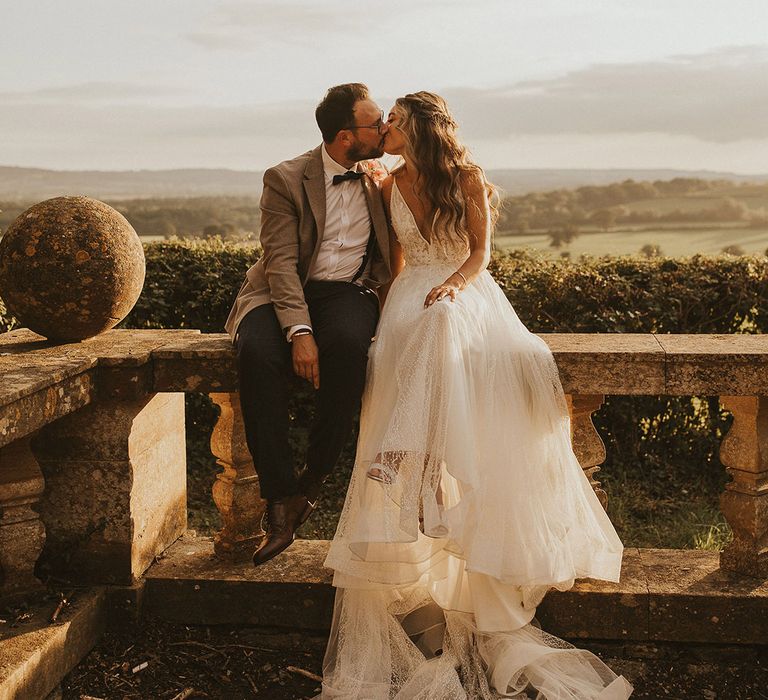 Bride & groom kiss as they sit on balcony outdoors on their wedding day