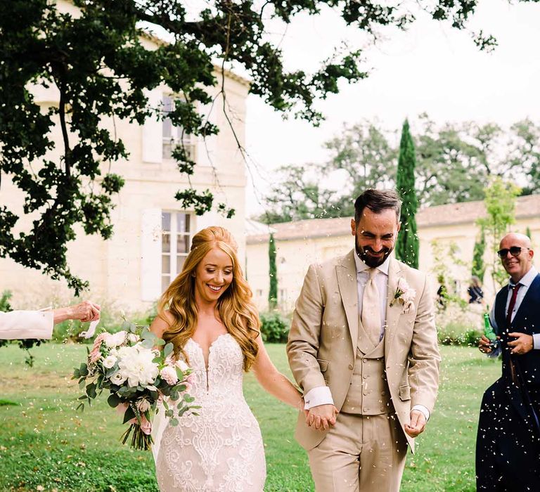 Bride & groom walk with one another as wedding guests throw confetti around them outdoors