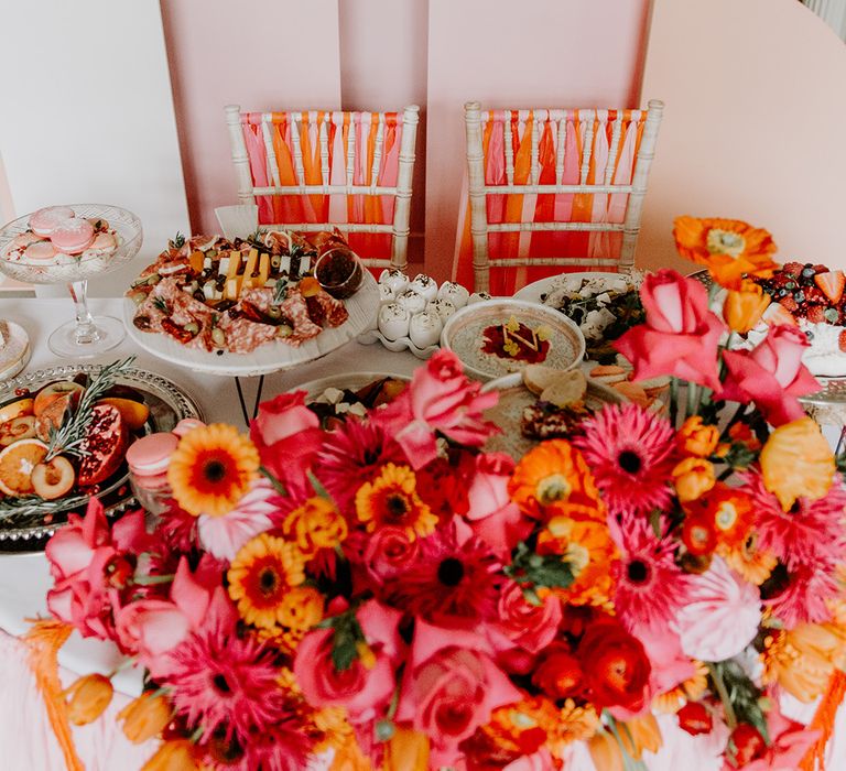 Sweetheart table with pink geometric backdrop, red, pink and orange flower arrangement and bistro food by Baba Ganoush 